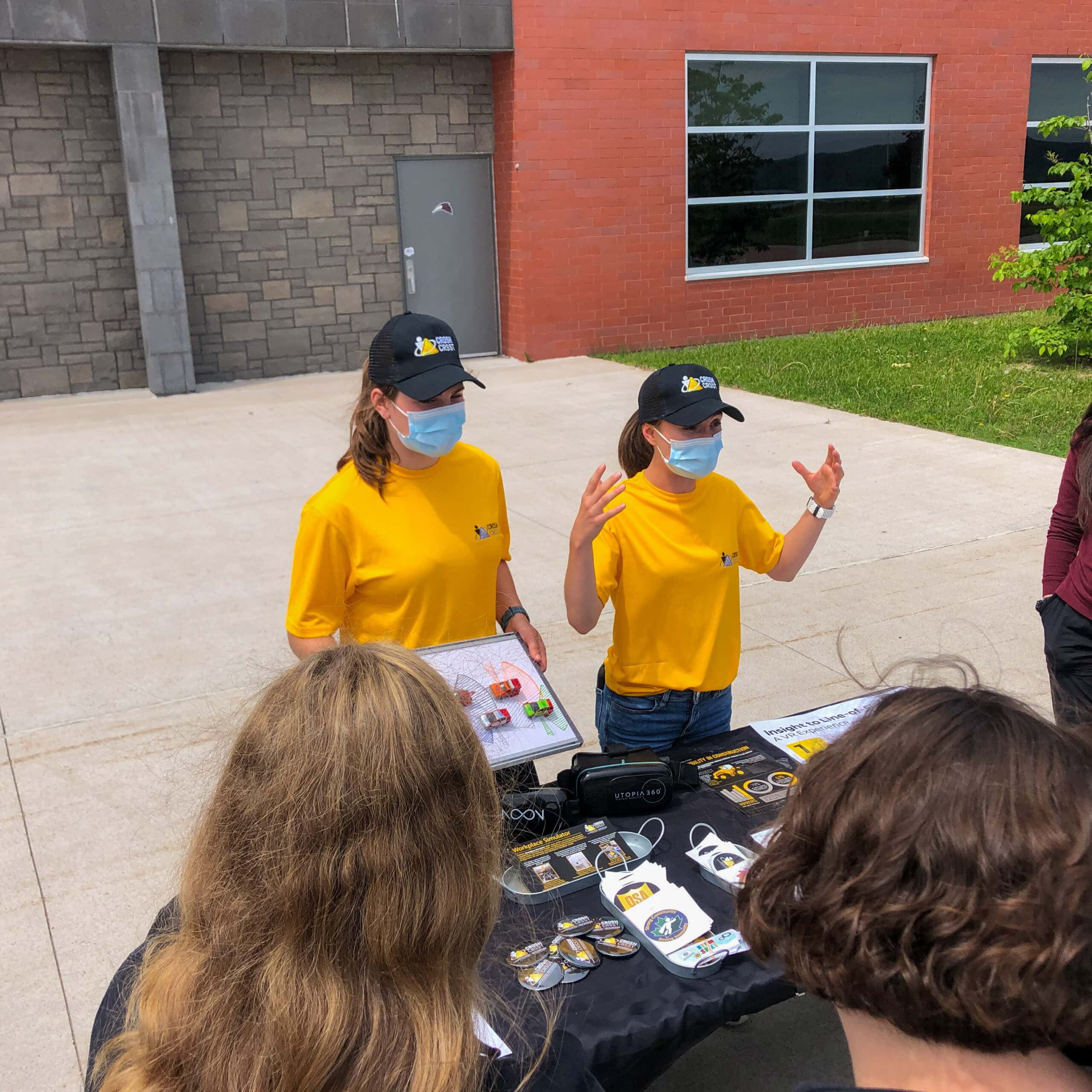 Two CROSH students explaining line-of-sight to high school students around a table outdoors