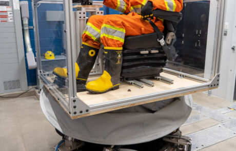 A worker in PPE wearing a VR headset and sitting in a simulated vehicle cab on top of a vibration platform